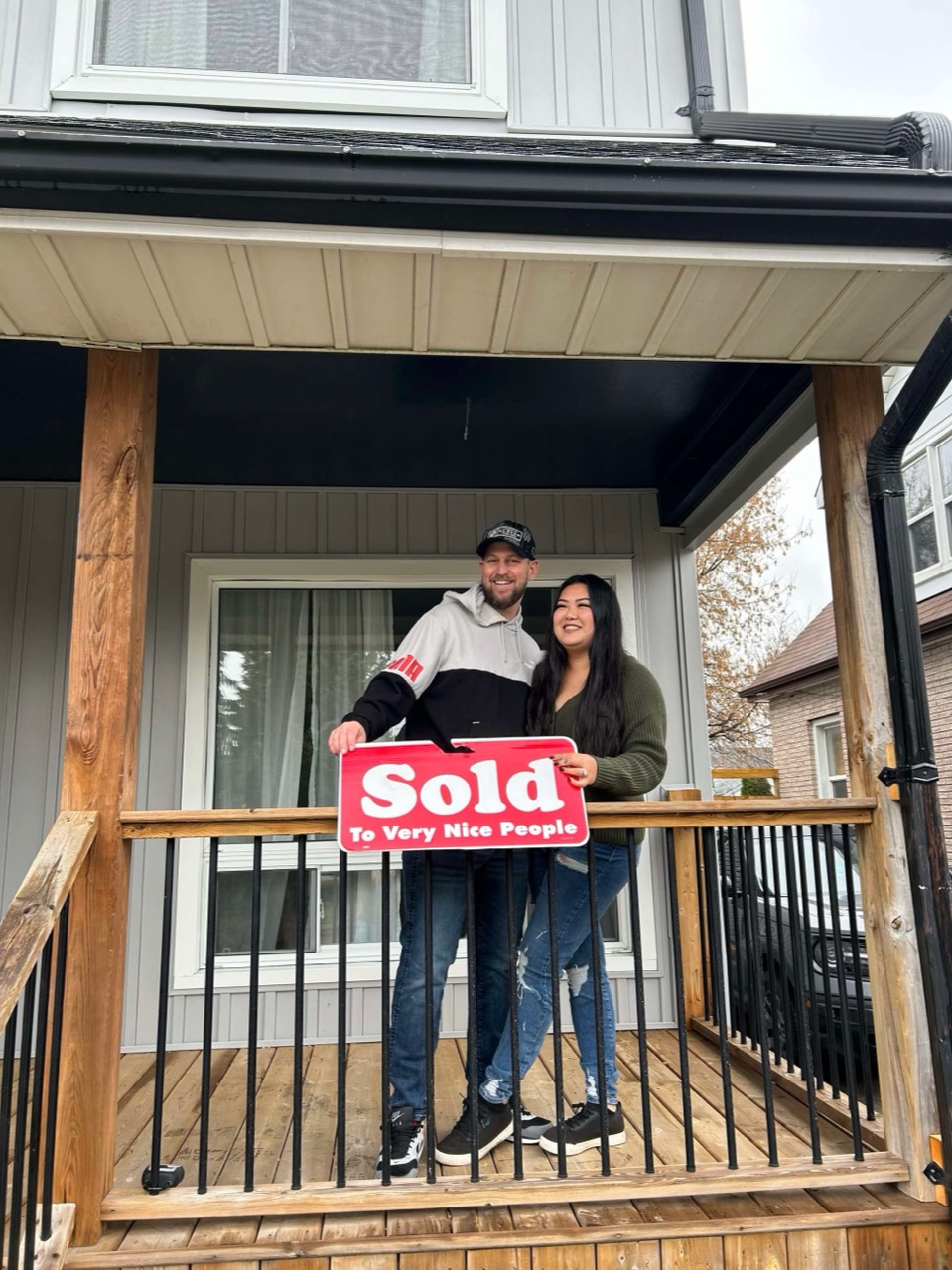 Two first-time buyers standing on the front porch holding a sold sign.